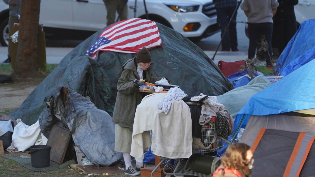 In this March 24, 2021, file photo, a woman eats at her tent at the Echo Park homeless encampment at Echo Park Lake in Los Angeles. (AP Photo/Damian Dovarganes, File)