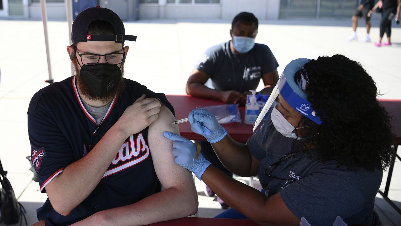Chandler Millard, left, of Alexandria, Va., receives a Johnson & Johnson vaccine at a COVID-19 vaccination clinic hosted by the Washington Nationals outside of Nationals Park before a baseball game against the Colorado Rockies, Saturday, Sept. 18, 2021, in Washington. (AP Photo/Nick Wass)