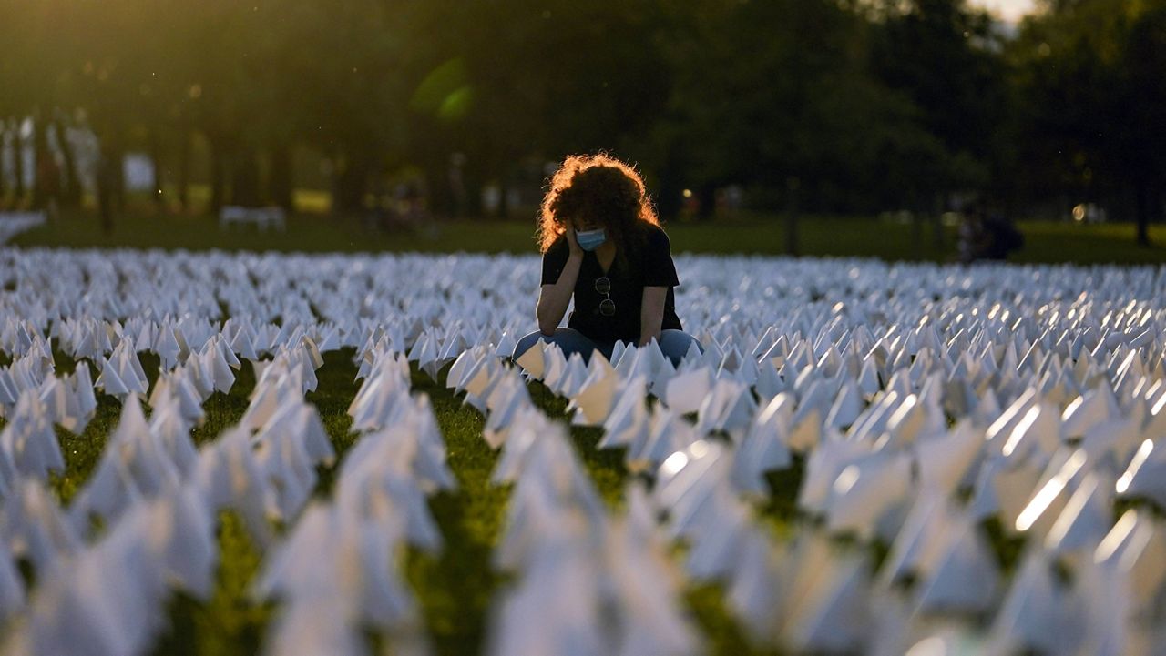 Zoe Nassimoff, whose grandparent died of COVID-19, looks at white flags on the National Mall in Washington, D.C., that are part of artist Suzanne Brennan Firstenberg's temporary art installation, "In America: Remember," in remembrance of Americans who have died from the virus. (AP Photo/Brynn Anderson, File)