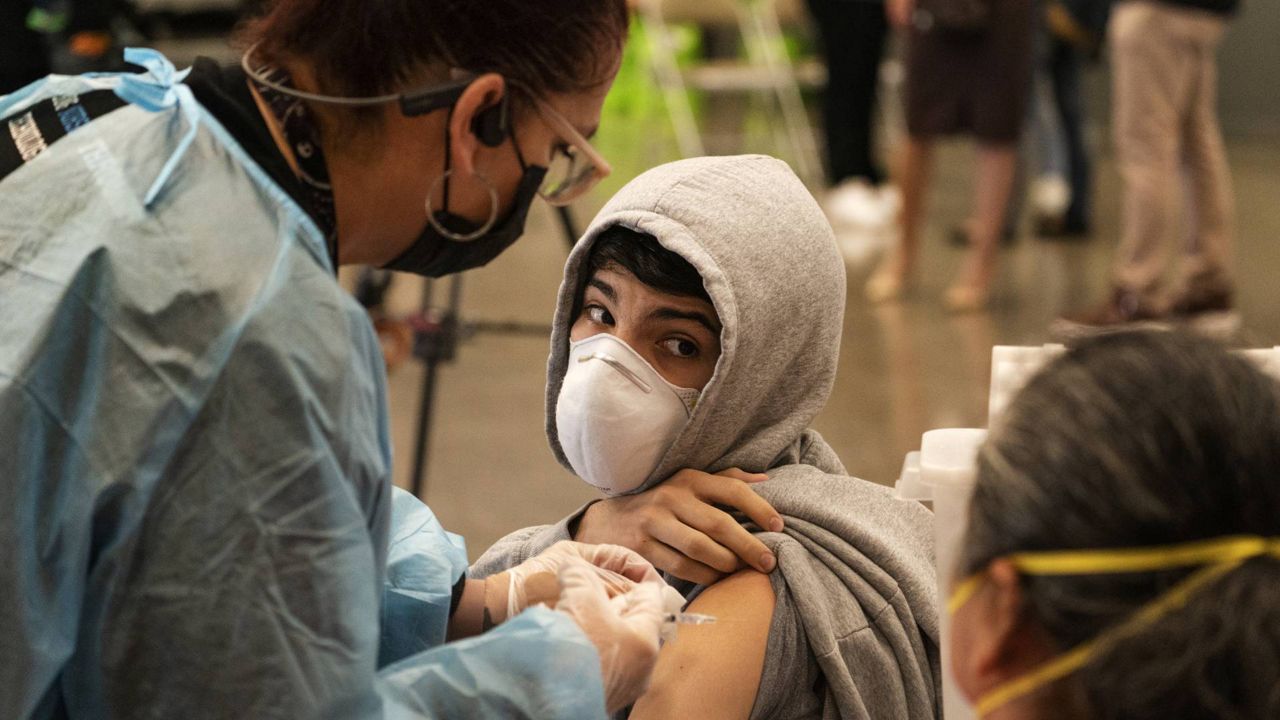 In this May 24, 2021, file photo, a student looks back at his mother as he is vaccinated at a school-based COVID-19 vaccination clinic for students 12 and older in San Pedro, Calif. (AP Photo/Damian Dovarganes)