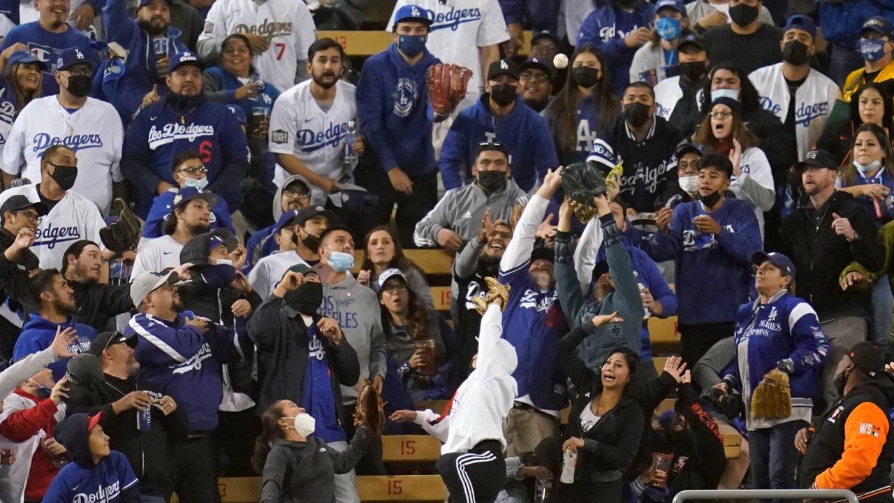 Fans in the stands at Dodger Stadium reach up to try and catch a solo home run hit during Game 3 of the National League Division Series, Oct. 11, 2021, in Los Angeles. (AP Photo/Ashley Landis)