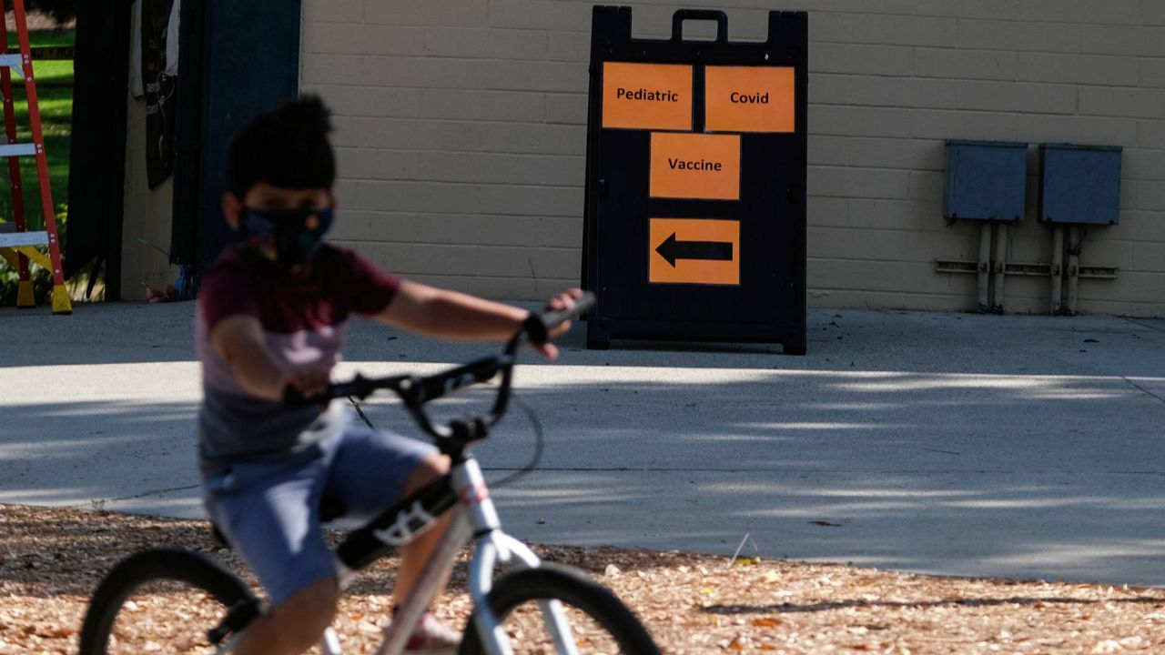 A boy rides his bike past a sign reading, "Pediatric Covid Vaccine" outside a COVID-19 vaccine center in Los Angeles, on Nov. 3, 2021. (AP Photo/Ringo H.W. Chiu)