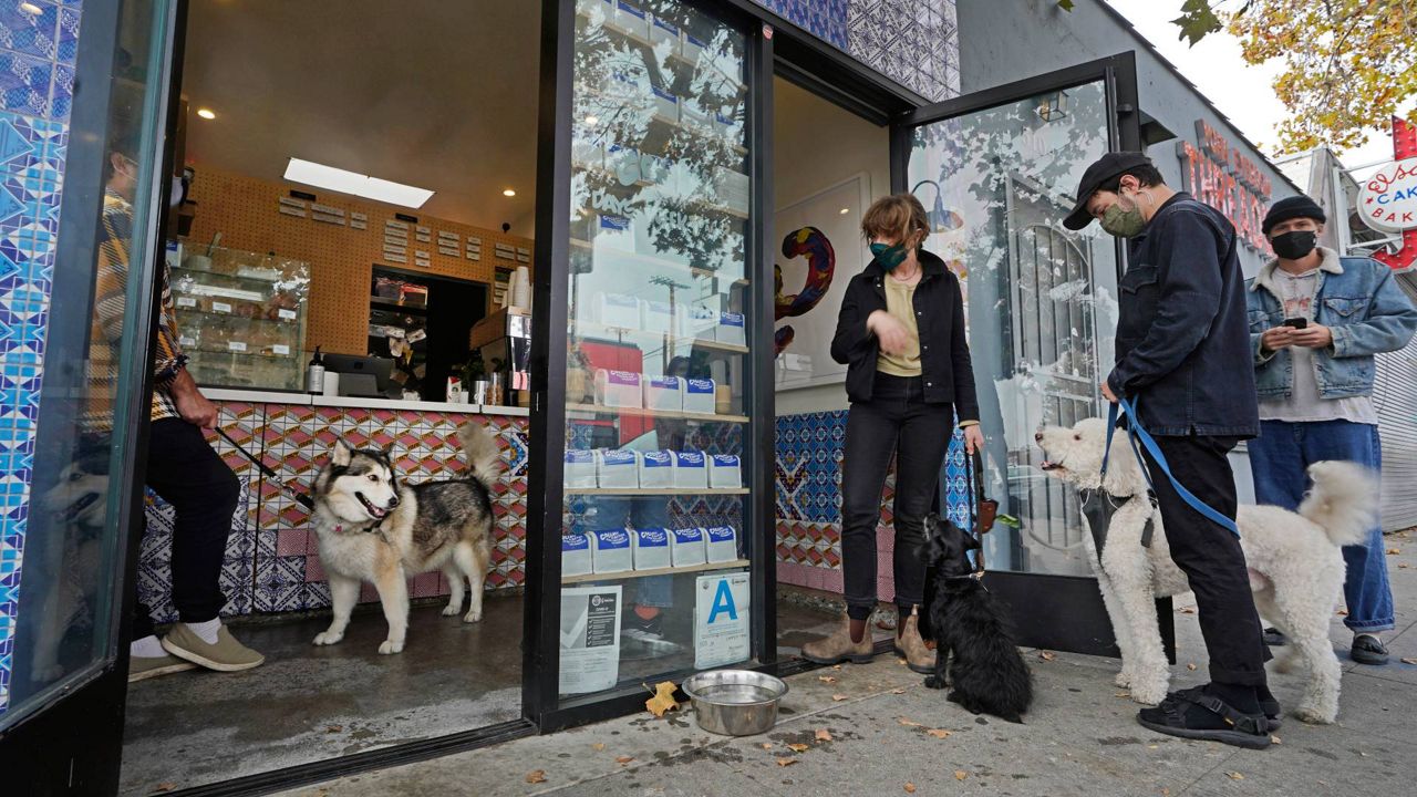 Patrons with their dogs keep their social distance while waiting in line outside Collage Cafe in the Highland Park neighborhood of Los Angeles, Saturday, Nov. 6, 2021. (AP Photo/Damian Dovarganes)