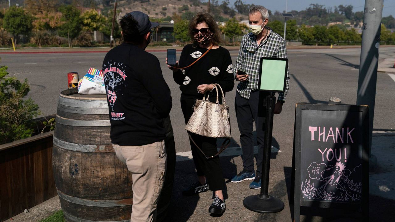 Marta McKay, center, and her husband, Bob, show a restaurant worker their proof of COVID-19 vaccination as they enter Highland Park Brewery, Nov. 8, 2021, in Los Angeles. (AP Photo/Jae C. Hong)