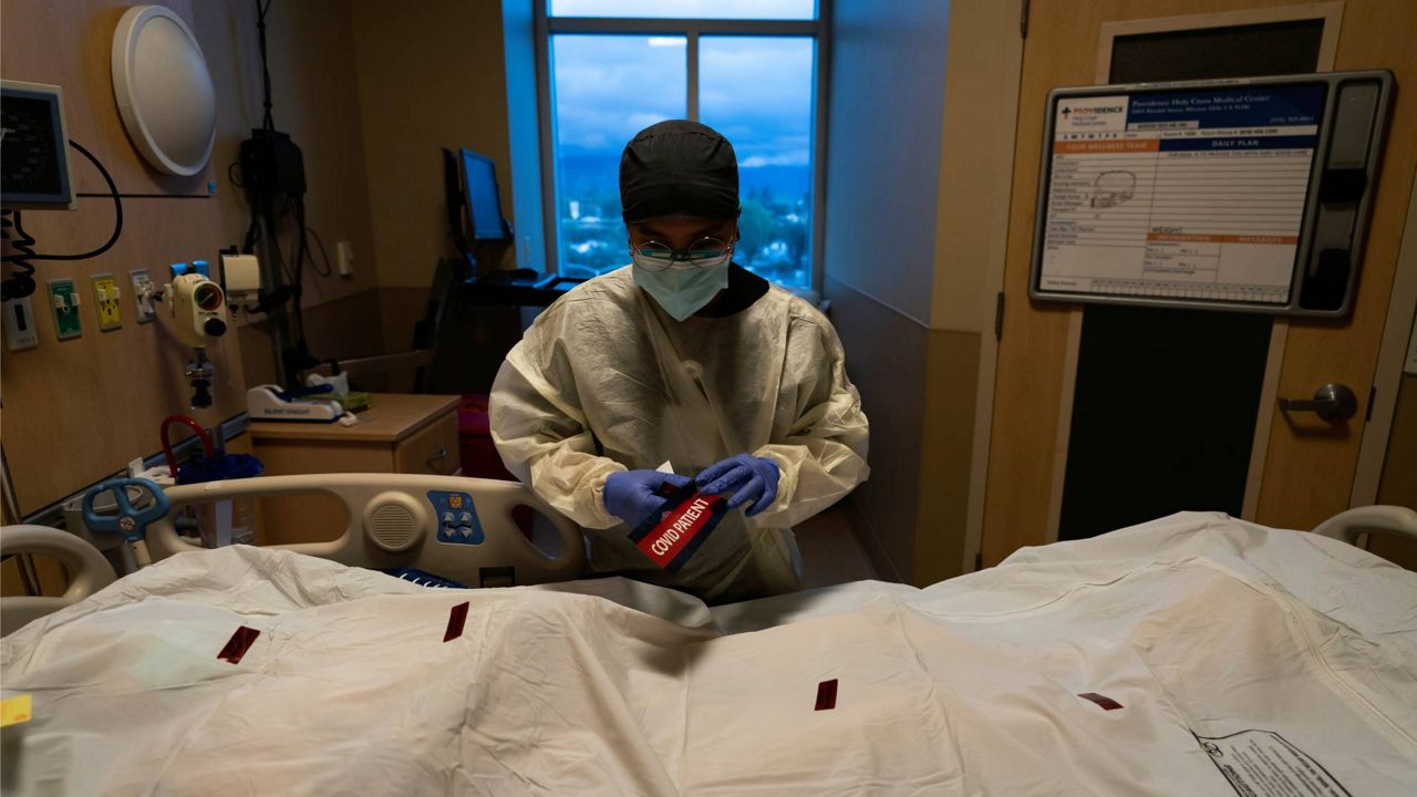 Registered nurse Bryan Hofilena attaches a "COVID Patient" sticker on a body bag of a patient who died of coronavirus at Providence Holy Cross Medical Center in Los Angeles, Tuesday, Dec. 14, 2021. (AP Photo/Jae C. Hong)