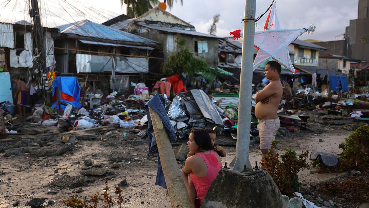 A family stands outside damaged homes due to Typhoon Rai in Surigao City, Philippines on Sunday. (AP Photo/Jilson Tiu)