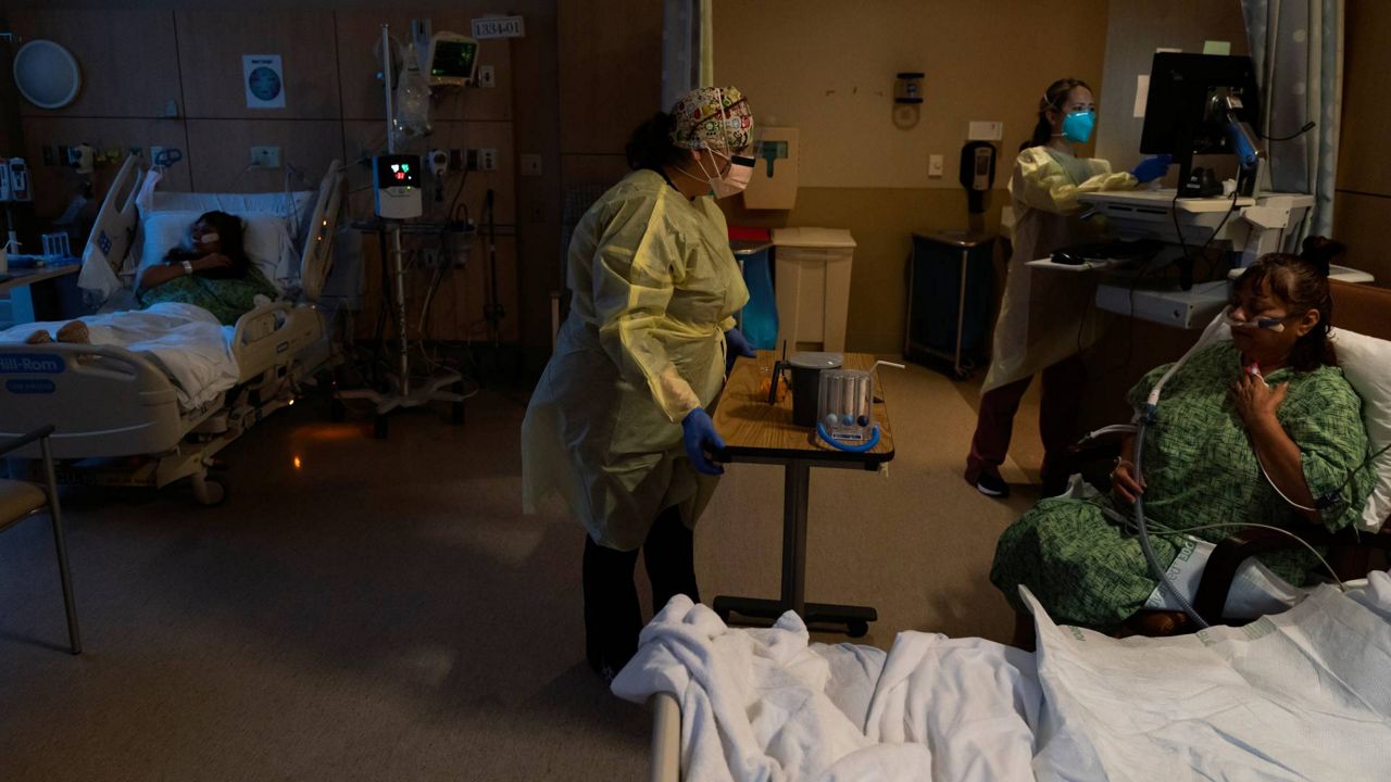 Registered nurse Nvard Termendzhyan, center, sets up a table for Linda Calderon, right, as her twin sister Natalie Balli, left, rests in her bed in a COVID-19 unit at Providence Holy Cross Medical Center in Los Angeles, Dec. 13, 2021. (AP Photo/Jae C. Hong, File)
