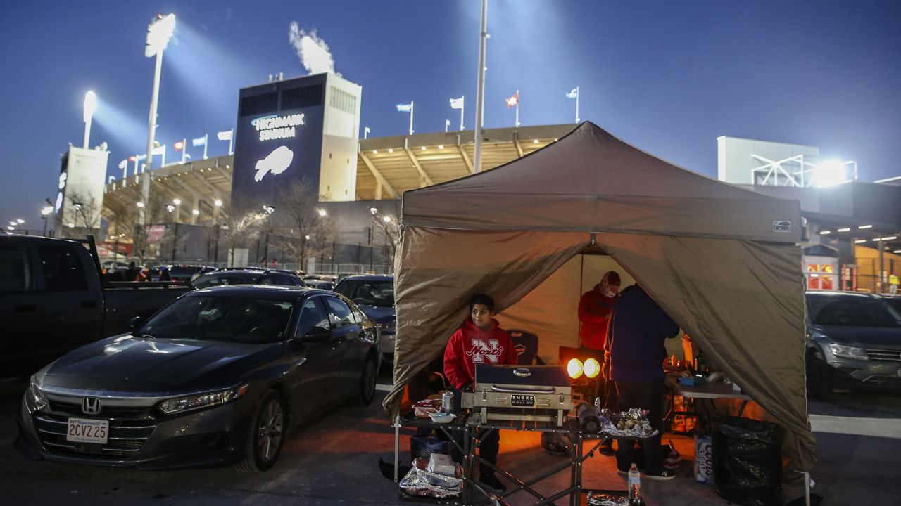 The Ammons and McFadden families tailgate inside a tent as temperatures drop in the parking lots outside of Highmark Stadium before an NFL wild-card playoff football game between the Buffalo Bills and the New England Patriots, Saturday, Jan. 15, 2022, in Orchard Park, N.Y. (AP Photo/Joshua Bessex)