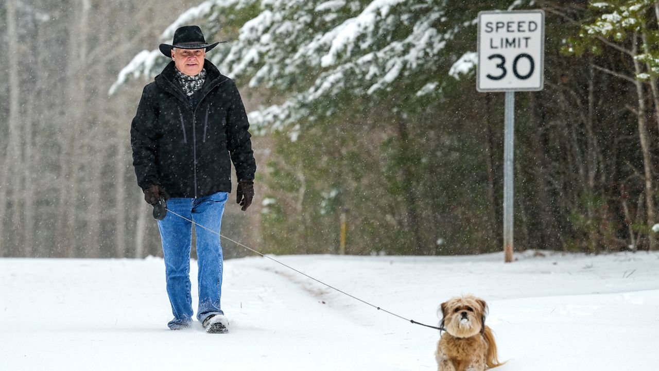 Paul Bossert walks his dog Winston through a snow-covered Southpointe Drive during a winter storm, Sunday, Jan. 16, 2022, in Morganton, N.C. (AP Photo/Kathy Kmonicek)