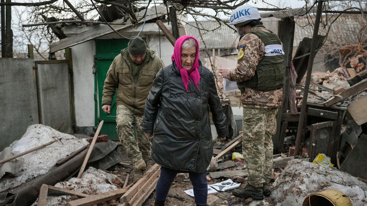 Valentyna Melnychenko walks with members of the Joint Centre for Control and Coordination on ceasefire of the demarcation line, or JCCC, who survey damage to her home from an artillery shell that landed in Vrubivka, one of the at least eight that hit the village today, according to local officials, in the Luhansk region, eastern Ukraine, Thursday, Feb. 17, 2022. (AP Photo/Vadim Ghirda)