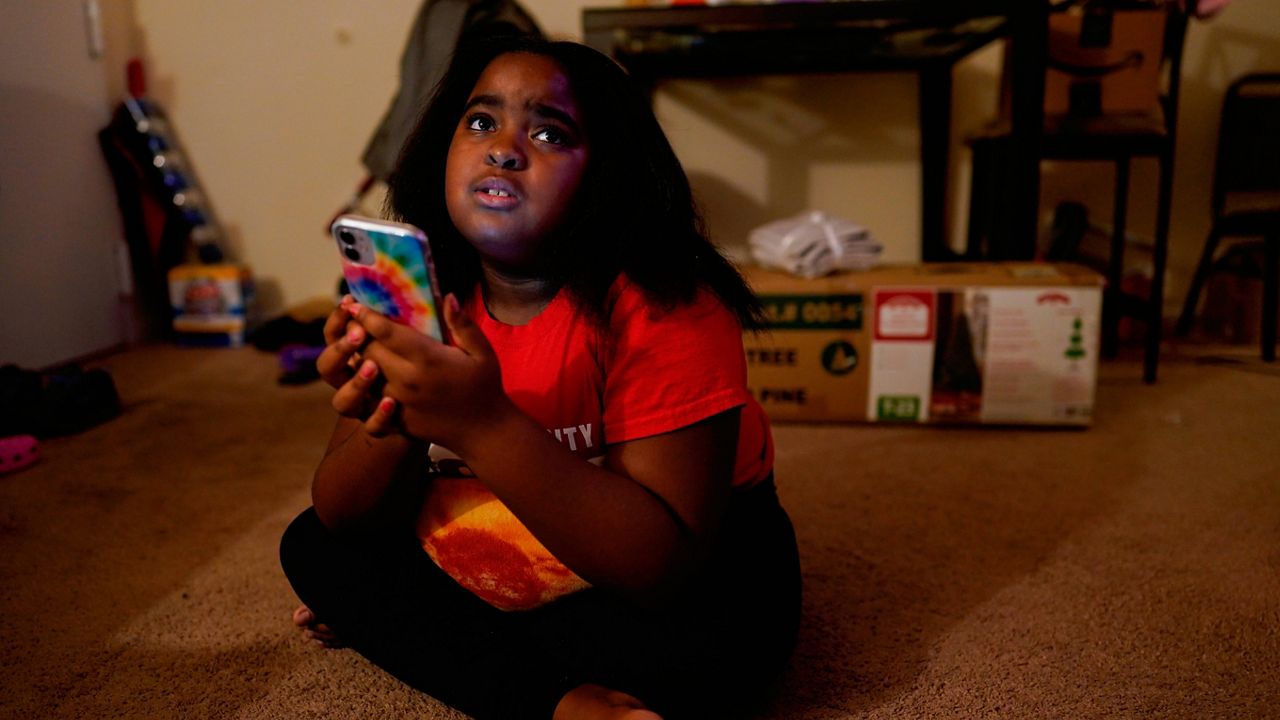 Brooklynn Chiles, 8, glances up from her smartphone at her home in Washington. Brooklynn lost her father to COVID-19 last year and has tested positive three times herself. (AP Photo/Carolyn Kaster)