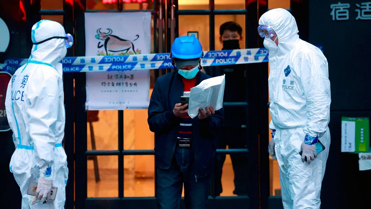 A delivery man walks by police officers with protective suit outside of a hotel in Shanghai, China, Tuesday.. (AP Photo)