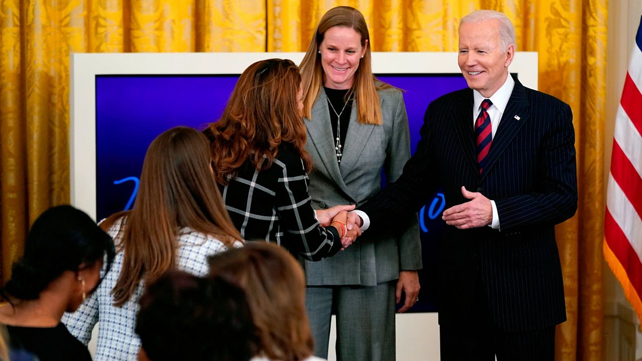 President Joe Biden invites onstage Cindy Parlow Cone, second from right, President of U.S. Soccer, along with current and former members of the U.S. Women's National Team during an event to celebrate Equal Pay Day and Women's History Month in the East Room of the White House, Tuesday, March 15, 2022, in Washington. (AP Photo/Patrick Semansky)