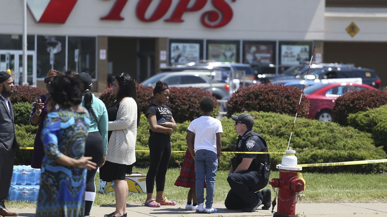 A Buffalo police officer talks to children at the scene of Saturday's shooting at a supermarket on Sunday, May 15, 2022, in Buffalo, N.Y. A white 18-year-old wearing military gear and livestreaming with a helmet camera opened fire with a rifle at a supermarket, killing and wounding people in what authorities described as “racially motivated violent extremism.” (AP Photo/Joshua Bessex)