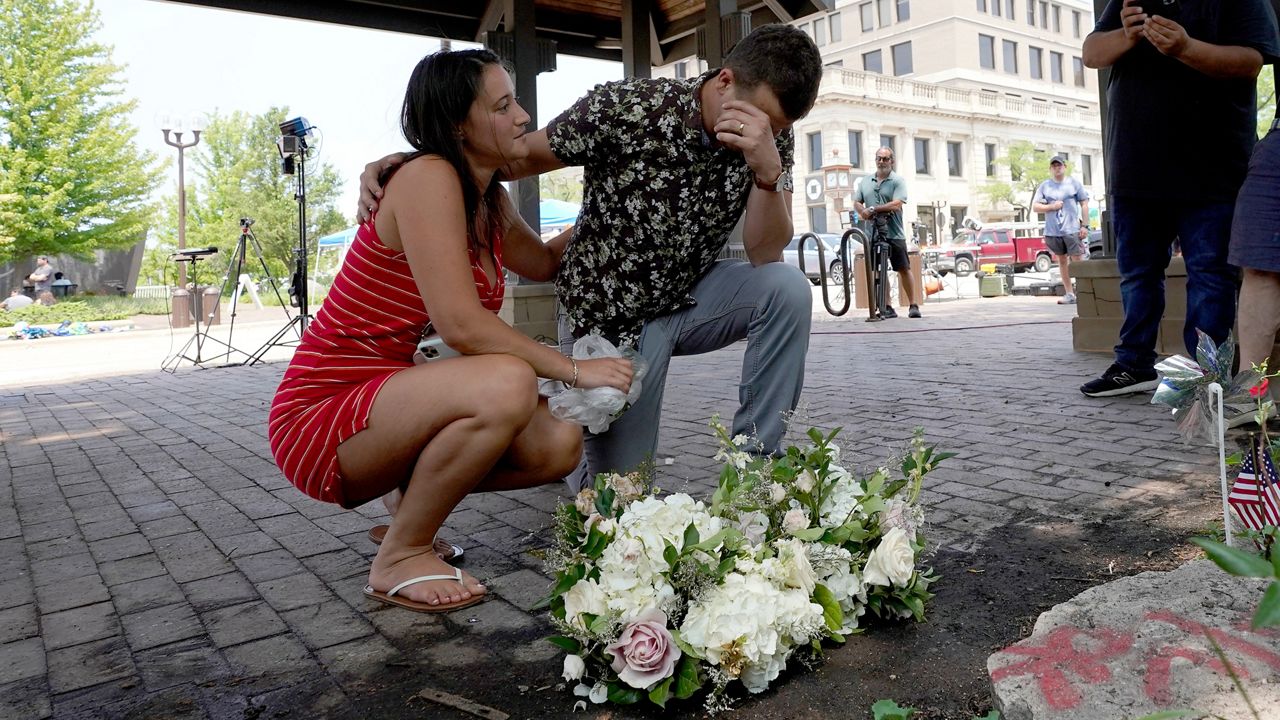 Brooke and Matt Strauss, who were married Sunday, pause after leaving their wedding bouquets in downtown Highland Park, Ill., near the scene of Monday's mass shooting Tuesday, July 5, 2022, in Highland Park, Ill. (AP Photo/Charles Rex Arbogast)