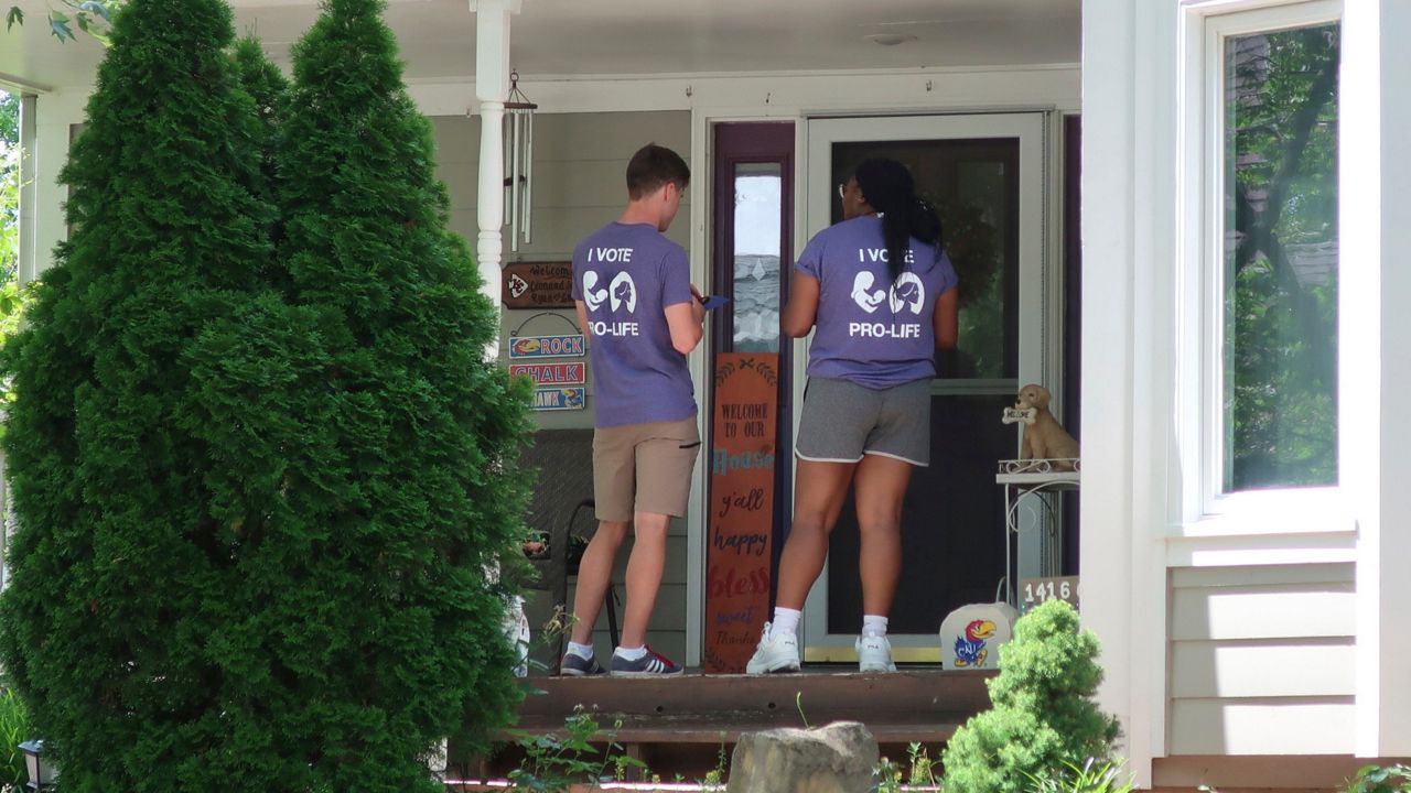 FILE - Ben Kennedy, left, and Alyssa Winters, left, wait at a door to speak with prospective voters about a proposed amendment to the Kansas Constitution that would allow legislators to further restrict or ban abortion, Friday, July 8, 2022, in Olathe, Kan. They are among about 300 college students brought into Kansas by the Susan B. Anthony Pro-Life America group, which backs the measure. (AP Photo/John Hanna, File)