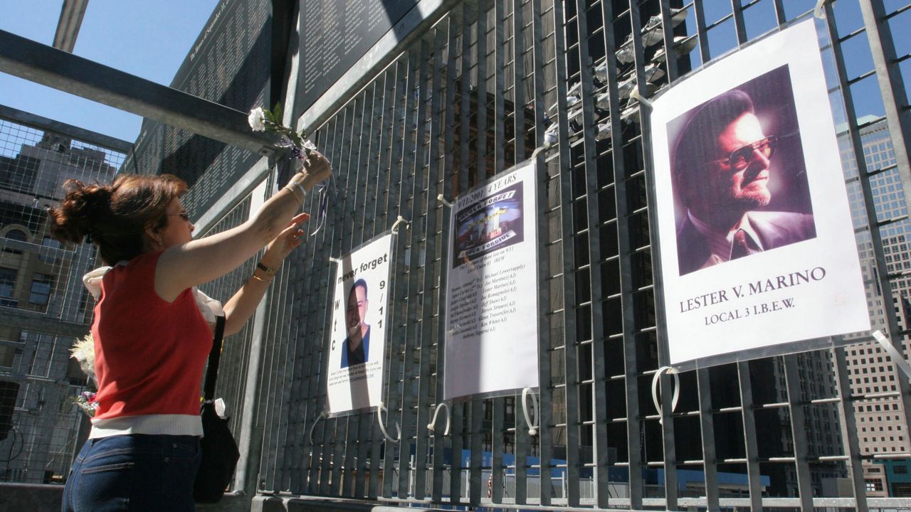 FILE - Kathy Haberman places a flower and card in memory of her daughter Andrea Haberman on a gate with other memorial images surrounding ground zero, the site where the World Trade Center once stood in New York, Saturday, Sept. 10, 2005. (AP Photo/Tina Fineberg, File)