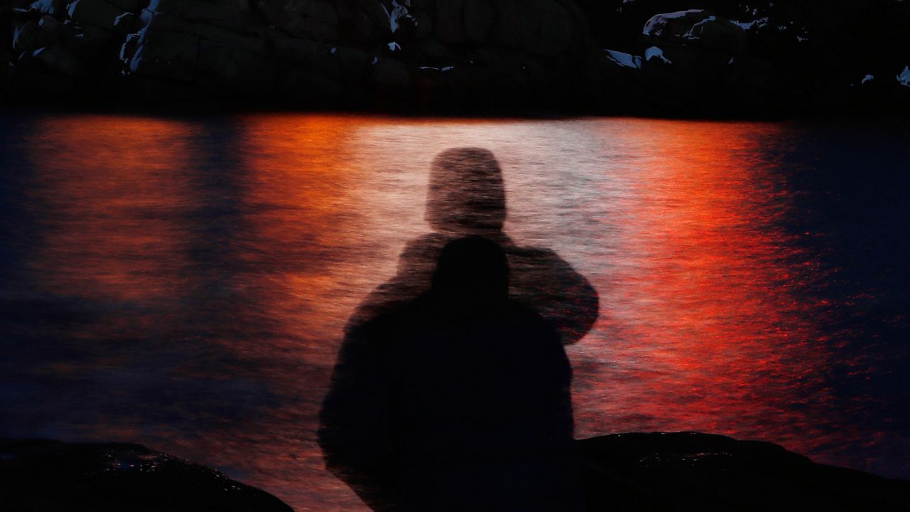 FILE - In this photo made with a long exposure, a man is silhouetted against lights reflected in the waters off Cape Neddick in Maine on Dec. 11, 2017. (AP Photo/Robert F. Bukaty, File)