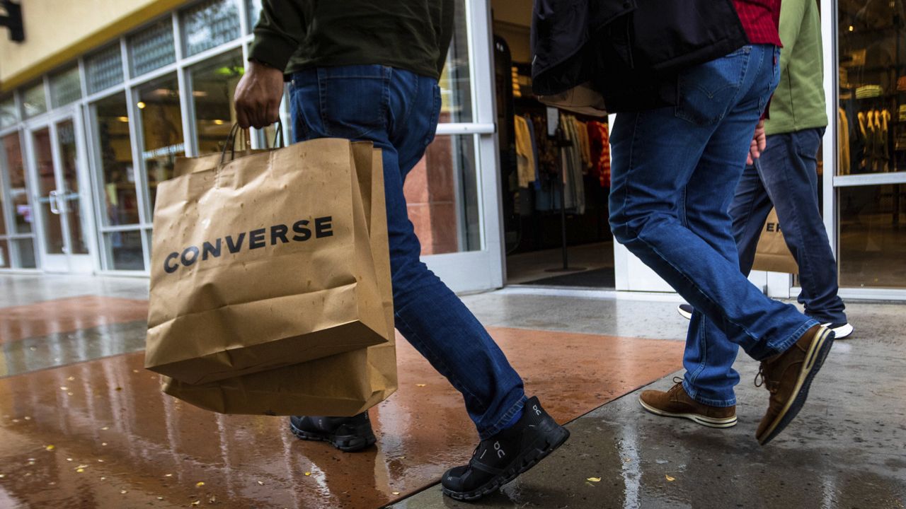 A shopper carries multiple bags while walking with others on Tuesday, March 14, 2023, in Las Vegas. (AP Photo/Ty O'Neil)