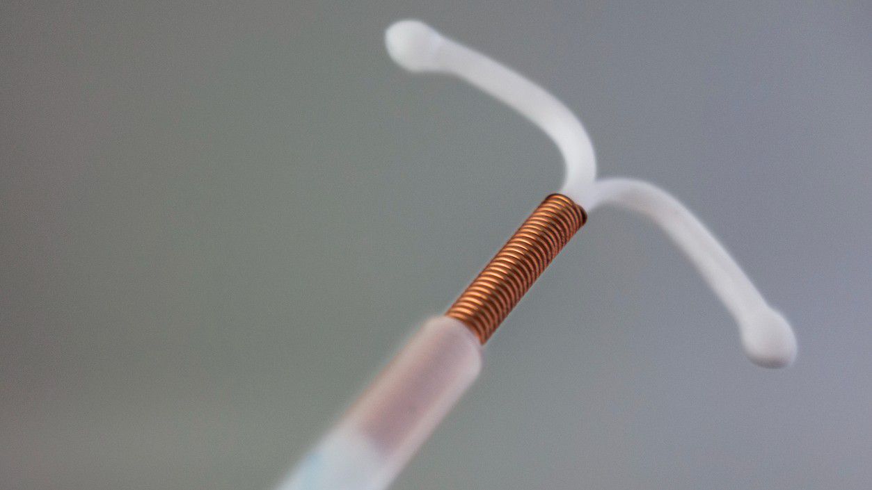 A copper IUD is shown against a grey background.