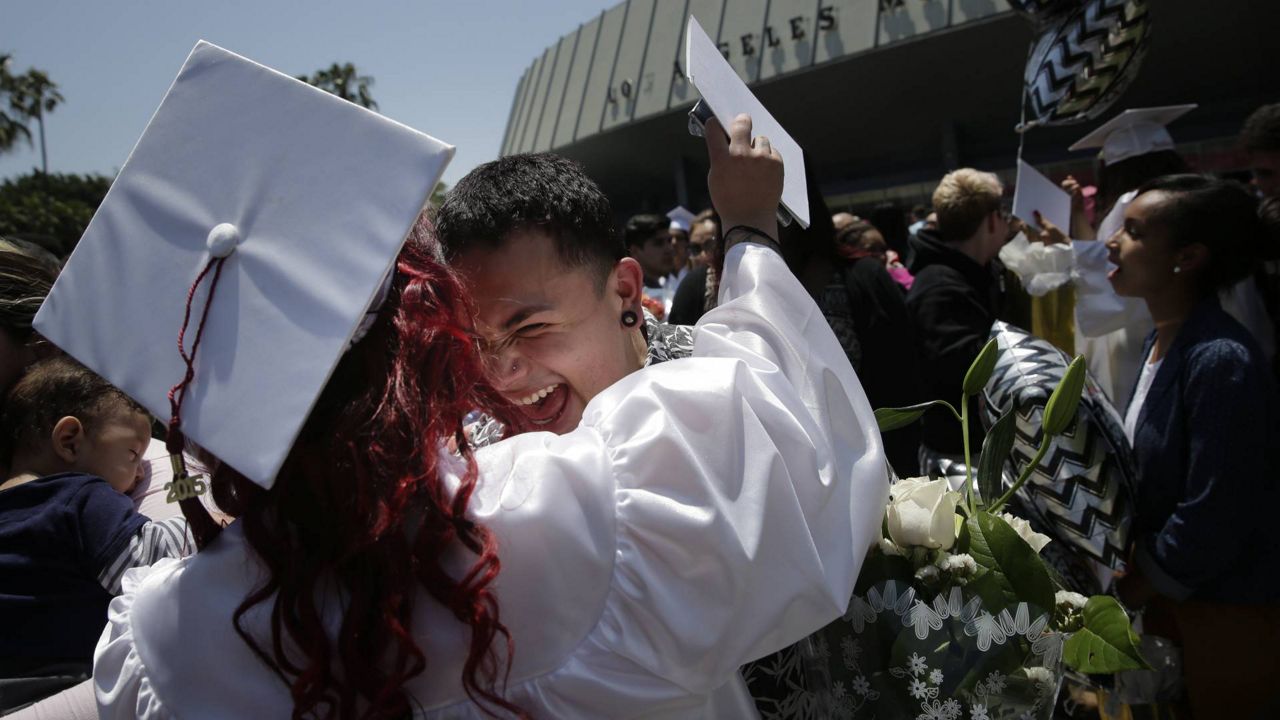 In this May 28, 2015 photo, wearing a cap and gown, Madison Rodriguez is congratulated by Jonathan Castro, center, at a graduation ceremony for students from continuation schools in LA. (AP Photo/Jae C. Hong)