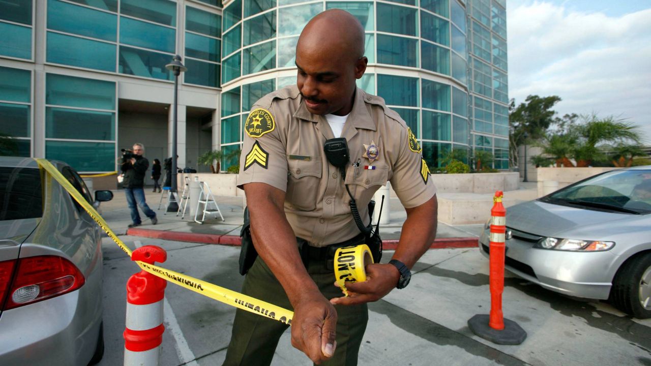 Los Angeles County Sheriff's Deputy Tony Taylor stretches yellow tape outside court on Dec. 12, 2012 in Los Angeles. (AP Photo/Nick Ut)