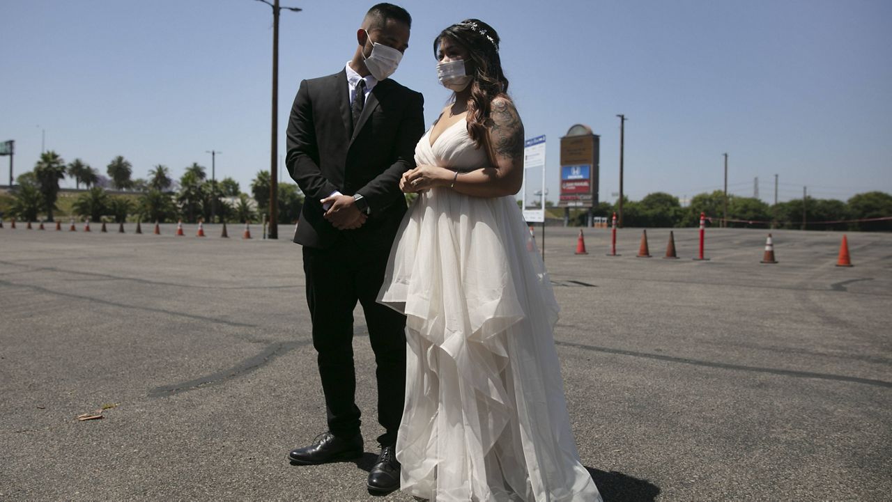 (AP Photo/Jae C. Hong) Roselle Querido, right, and her bridegroom Mo de las Alas wait for their marriage service to begin in the parking lot of the Honda Center in Anaheim, Calif., Tuesday, May 26, 2020. 