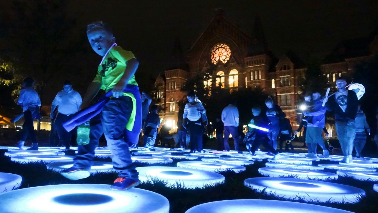 Revelers interact with the luminescent pressure-triggered platforms of an art installation in Washington Park during the Blink Festival, Thursday, Oct. 12, 2017, in Cincinnati. Blink, an evening art exhibition, features light shows and projections on structures throughout downtown Cincinnati as well as interactive installations. (AP Photo/John Minchillo)