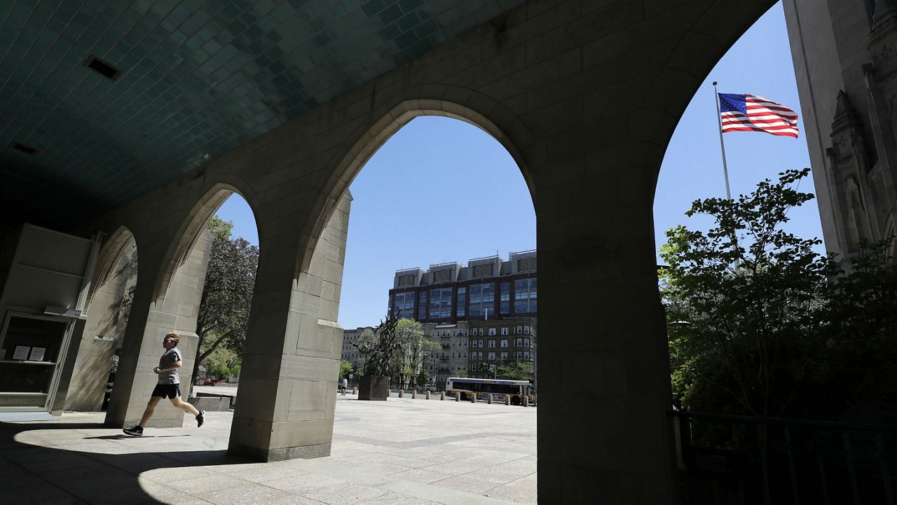 In this Wednesday, May 20, 2020 photo a runner passes through an arch on the campus of Boston University, in Boston. Boston University is among a growing number of universities making plans to bring students back to campus this fall, but with new measures meant to keep the coronavirus at bay. (AP Photo/Steven Senne)