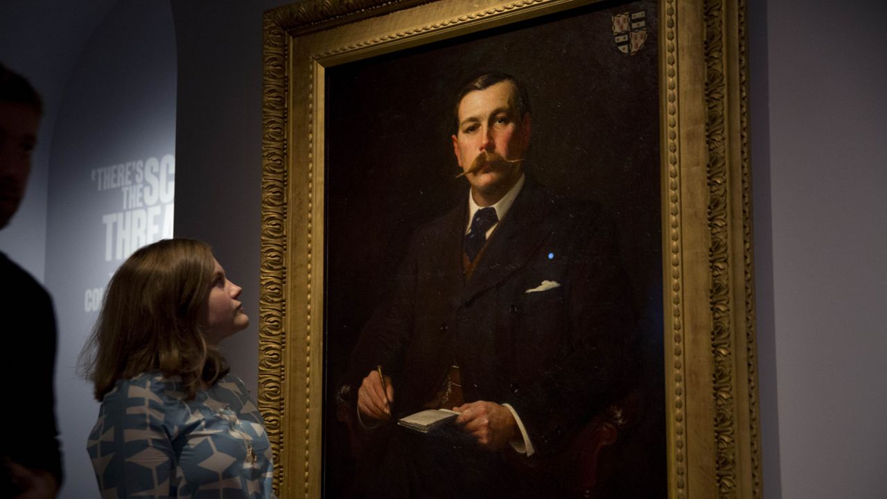 A Museum of London employee poses for photographers next to an 1897 oil on canvas portrait of Sherlock Holmes author Sir Arthur Conan Doyle by illustrator Sidney Paget on display as part of the exhibition "Sherlock Holmes: The Man Who Never Lived and Will Never Die" at the Museum of London in London, Oct. 16, 2014. (AP Photo/Matt Dunham, File)