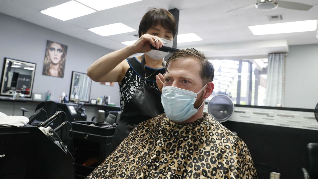 Amid concerns of the spread of COVID-19, Joe Farley, front, wears a mask as he gets a haircut from Kim at the just reopened Salon A la Mode in Dallas, Friday, April 24, 2020. (AP Photo/LM Otero)