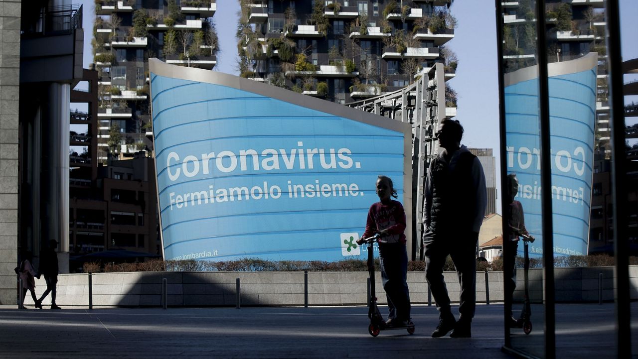 A man and a girl on a scooter are backdropped by a Lombardy region campaign advertising reading in Italian ' Coronavirus let's stop it together ', at the Porta Nuova business district in Milan, Wednesday, March 11, 2020. Italy is mulling even tighter restrictions on daily life and has announced billions in financial relief to cushion economic shocks from the coronavirus. For most people, the new coronavirus causes only mild or moderate symptoms, such as fever and cough. For some, especially older adults and people with existing health problems, it can cause more severe illness, including pneumonia. (AP Photo/Luca Bruno)