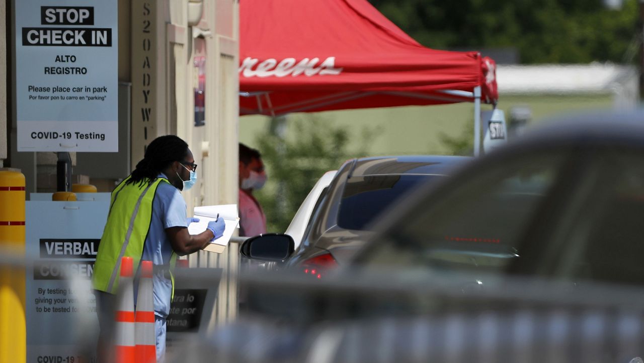 A slow but consistent flow of vehicles line up in a drive-thru area as a Walgreens pharmacist assists them with COVID-19 testing in Dallas, Saturday April 25, 2020. (AP Photo/Tony Gutierrez)