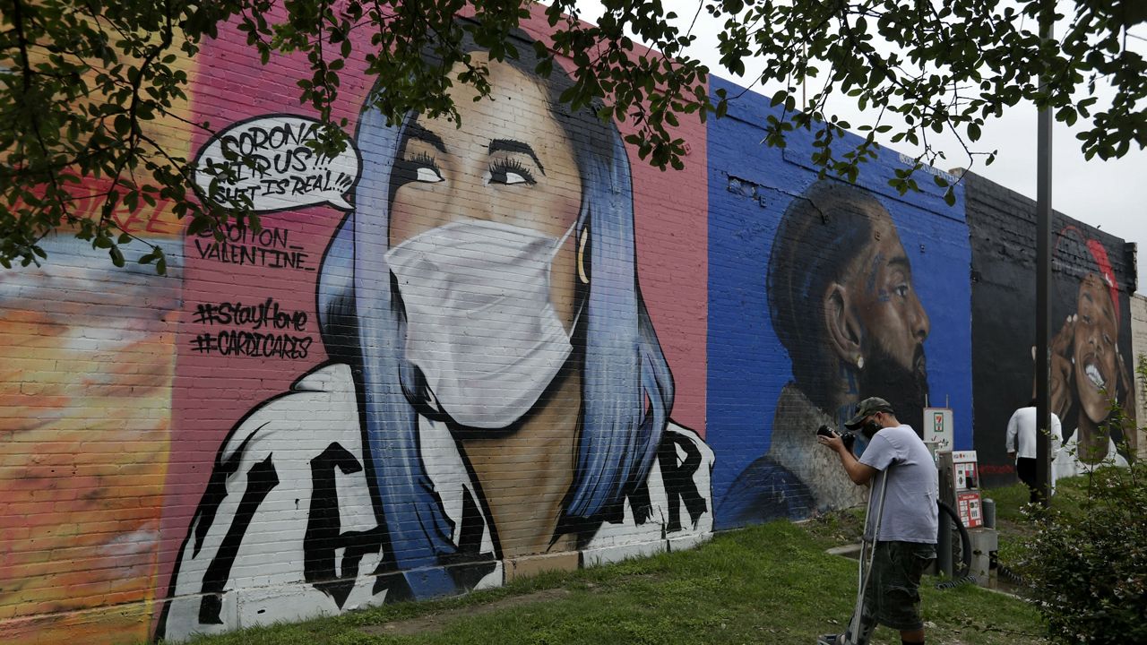 A man photographs a mural of Cardi B that was updated by the artist Colton Valentine to include a face mask to reflect the coronavirus pandemic, in San Antonio, Monday, March 30, 2020. (AP Photo/Eric Gay)