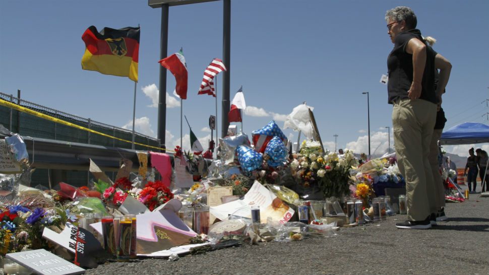 In this Aug. 12, 2019 photo, mourners visit the makeshift memorial near the Walmart in El Paso, Texas, where 22 people were killed in a mass shooting that police are investigating as a terrorist attack targeting Latinos. The flags show the nationalities of those killed in the attack, including a German man who lived in nearby Ciudad Juarez, Mexico. On Thursday, Aug. 22, 2019, Walmart said it plans to reopen the El Paso store where 22 people were killed in a mass shooting, but the entire interior of the building will first be rebuilt. (AP Photo/Cedar Attanasio)