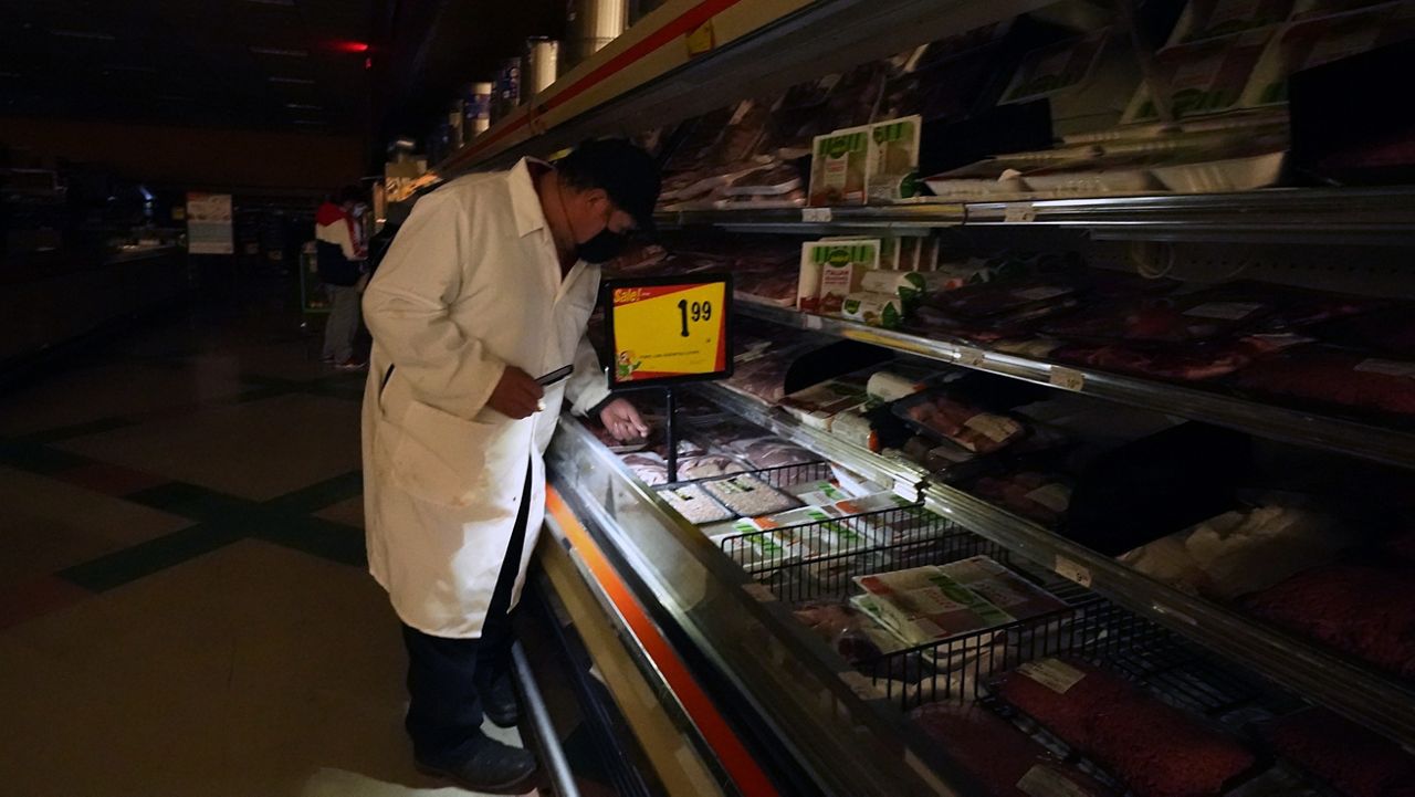 Raul Alonzo uses the light from a cell phone to arrange products in the meat section of a grocery store in Dallas in this image from February 2021. (AP Photo/LM Otero)