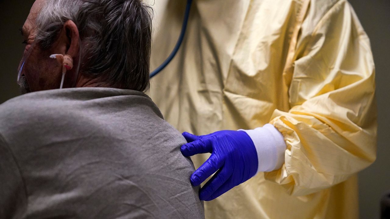 A medical professional rests their hand on a patient's back as they check the patient's heartbeat.