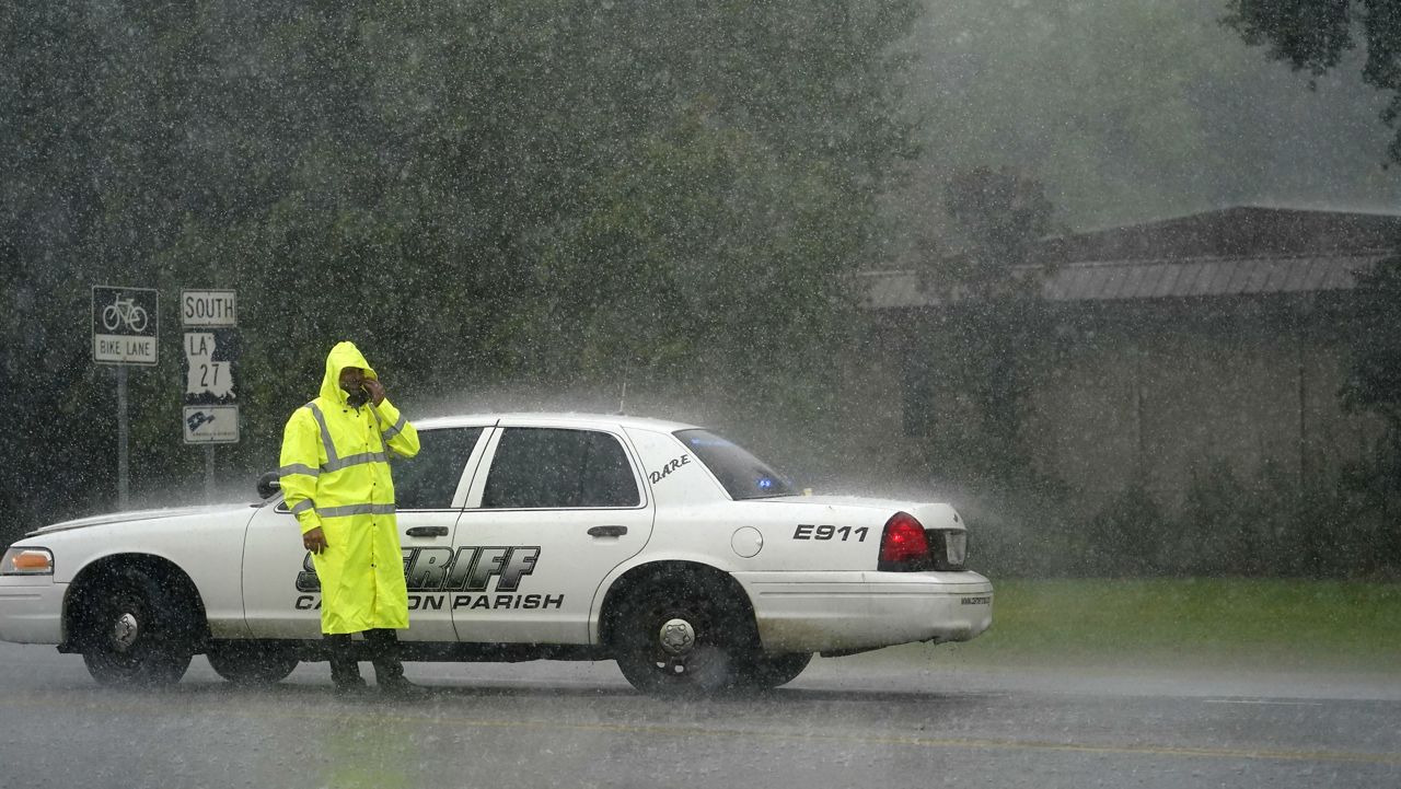 A Cameron Parish Sheriff deputy wipes his face as he mans a roadblock in the rain on LA 27 while residents evacuate Cameron in Lake Charles, La., Wednesday, Aug. 26, 2020, ahead of Hurricane Laura. (AP Photo/Gerald Herbert)