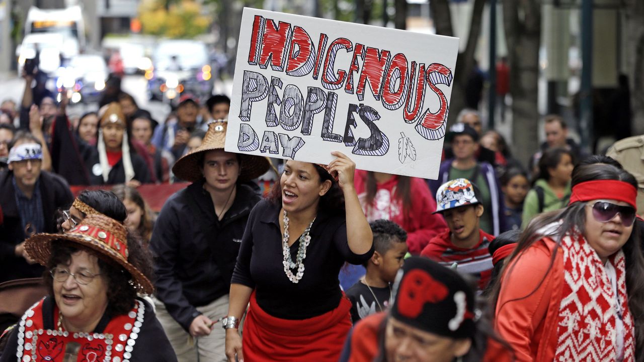 FILE - Miriam Zmiewski-Angelova, center, holds a sign for Indigenous Peoples Day during a demonstration and march, Monday, Oct. 12, 2015, in Seattle. (AP Photo/Elaine Thompson)