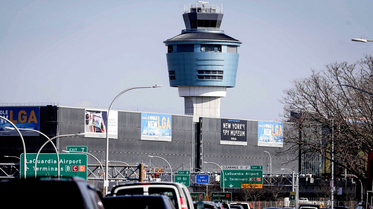 A photo of LaGuardia Airport's air traffic tower, with a highway and building also in the foreground.