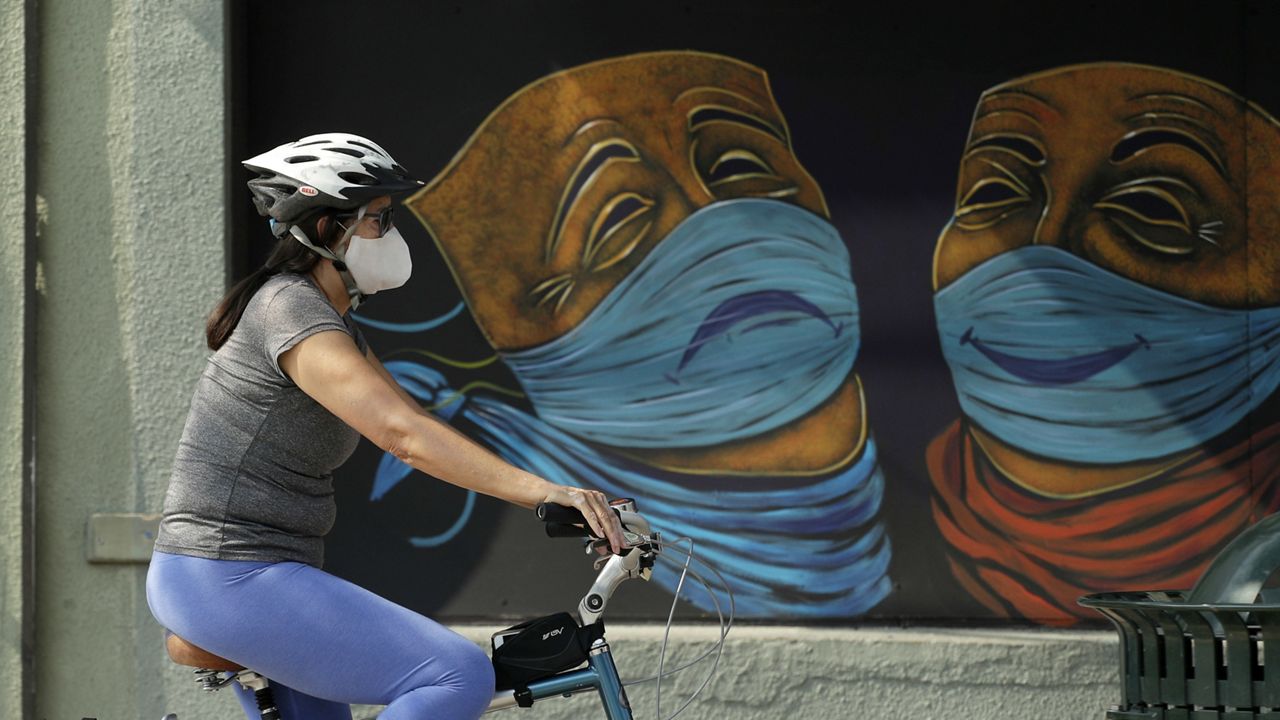 A woman bikes past a mural painted on a closed business, Tuesday, May 5, 2020, in Austin, Texas. (AP Photo/Eric Gay)