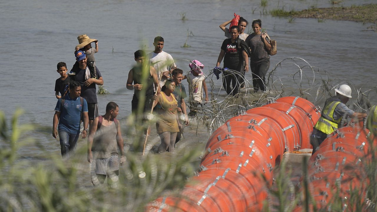 Migrantes que intentan ingresar a EE. UU. desde México se acercan al sitio donde los trabajadores ensamblan grandes boyas que se utilizarán como barrera fronteriza a lo largo de las orillas del Río Grande en Eagle Pass, Texas, el martes 11 de julio de 2023. (Foto AP/Eric Gay)