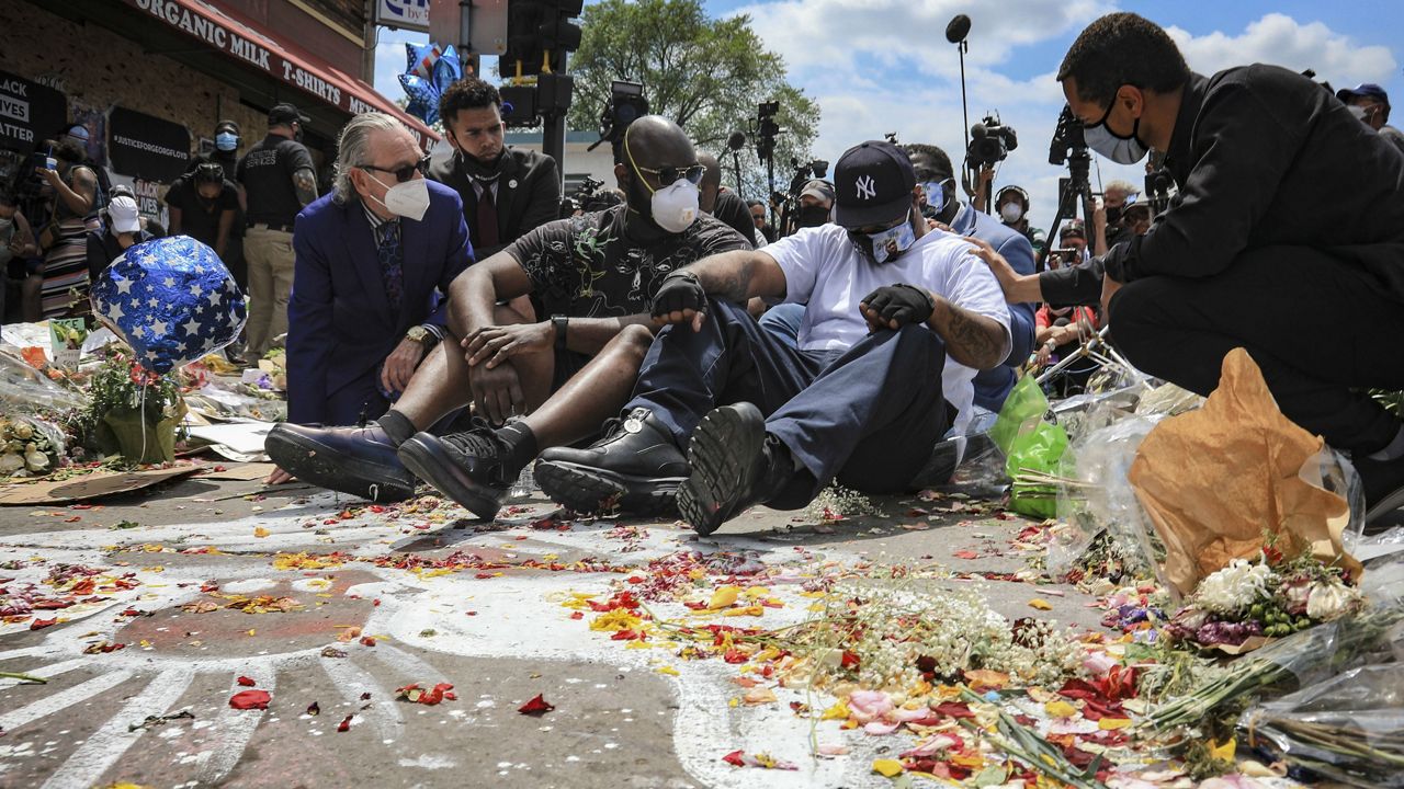 An emotional Terrence Floyd, second from right, is comforted as he sits at the spot at the intersection of 38th Street and Chicago Avenue, Minneapolis, Minn., where his brother George Floyd, encountered police and died while in their custody, Monday, June 1, 2020. (AP Photo/Bebeto Matthews)