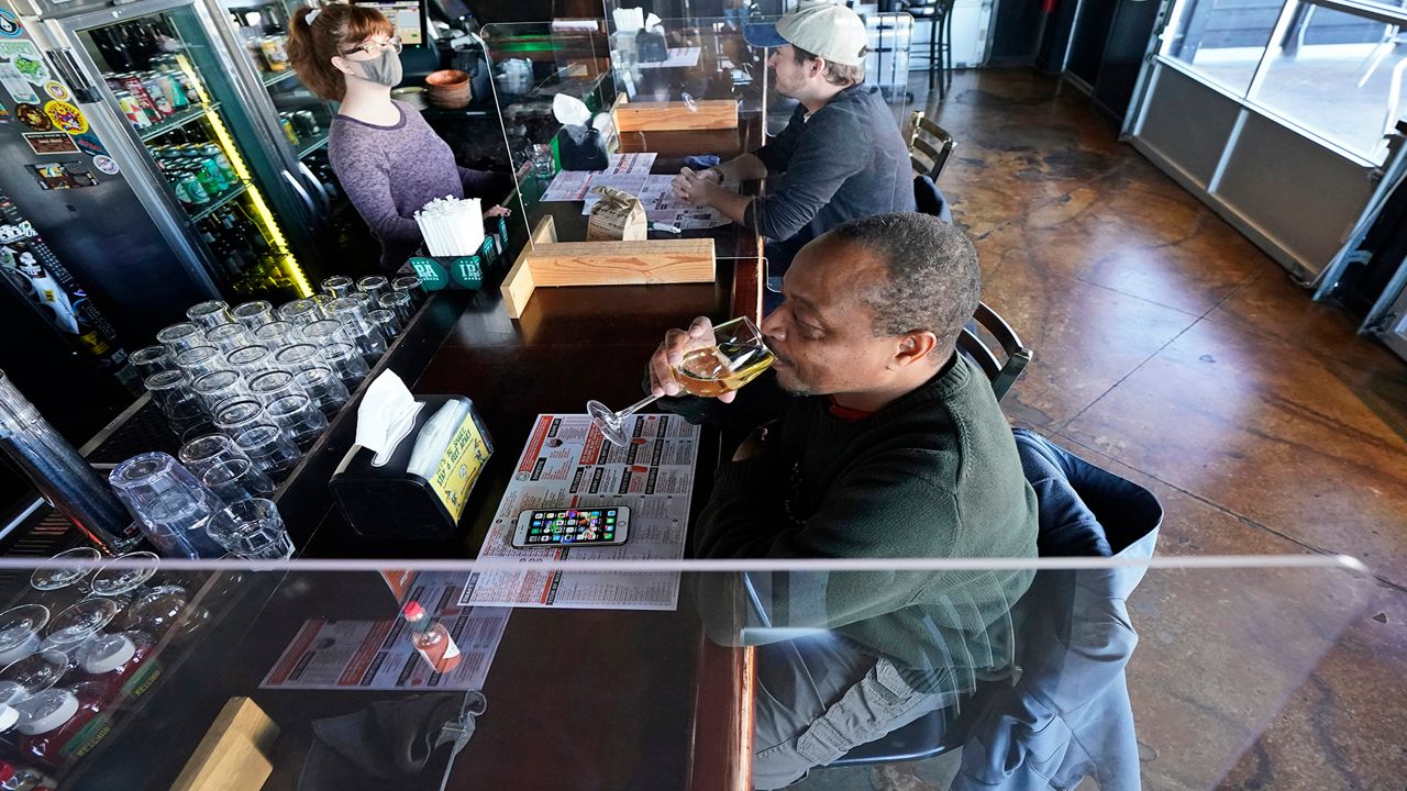 A man drinking at a bar separated by plastic barriers to protect against the spread of COVID-19