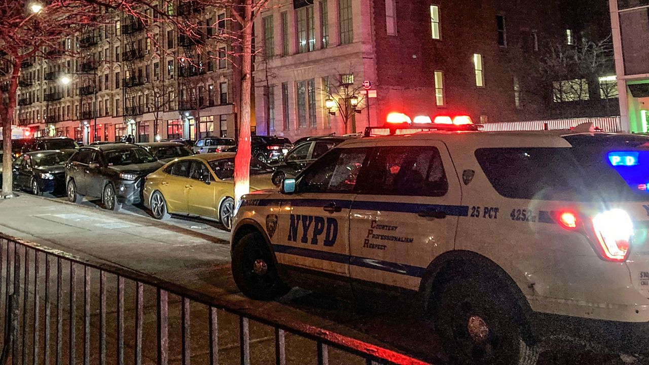 NYPD car with sirens going parked on sidewalk at night.