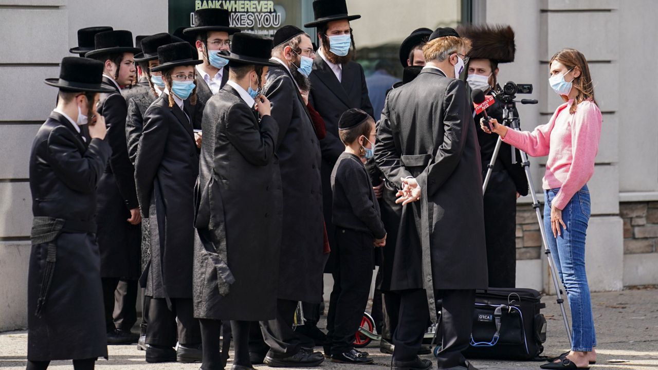 Members of the Jewish Orthodox community gather to listen to an interview conducted by a journalist on a street corner, Wednesday, Oct. 7, 2020, in the Borough Park neighborhood of the Brooklyn borough of New York. Gov. Andrew Cuomo moved to reinstate restrictions on businesses, houses of worship and schools in and near areas where coronavirus cases are spiking. Many neighborhoods that stand to be affected are home to large enclaves of Orthodox Jews. (AP Photo/John Minchillo)