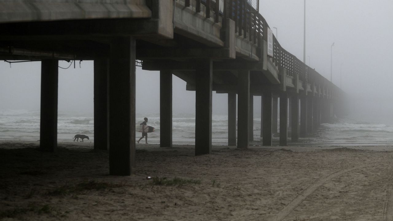 A surfer walks along the beach in an early morning fog, Monday, March 23, 2020, in Port Aransas, Texas. (AP Photo/Eric Gay)
