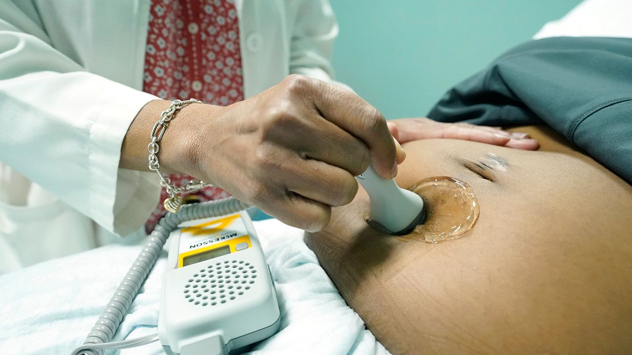 Dr. Felecia Brown, a midwife at Sisters in Birth, a Jackson, Miss., clinic that serves pregnant women, left, uses a hand held doppler probe on Kamiko Farris of Yazoo City, to measure the heartbeat of the fetus, Dec. 17, 2021. (AP Photo/Rogelio V. Solis)