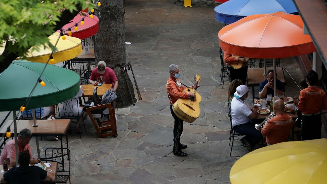 A man with a guitar and a face mask plays the guitar to patrons on the River Walk in downtown San Antonio (AP Image/File)