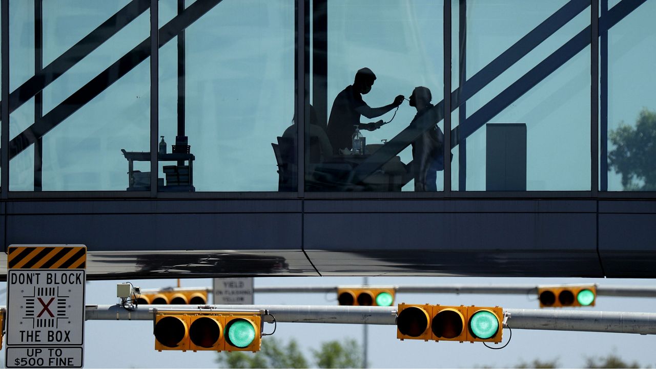 A woman has her temperature taken at a control point on a covered footbridge to be screened for symptoms before entering the Dell Deton Medical Center at the University of Texas in Austin, Texas, Wednesday, March 25, 2020. (AP Photo/Eric Gay)
